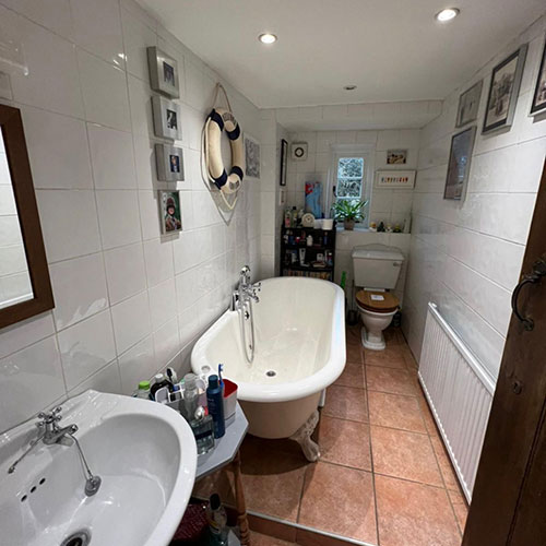 A before picture of a long thin customer bathroom with a bath, toilet and sink